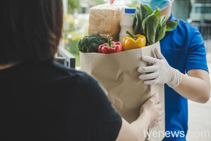 food-delivery-service-man-blue-uniform-wearing-protection-face-mask-holding-fresh-food-set-bag-customer-door-home-express-delivery-quarantine-virus-outbreak-takeaway-food-delivery-concept food delivery service man blue uniform wearing protection face mask holding fresh food set bag customer door home express delivery quarantine virus outbreak takeaway food delivery concept