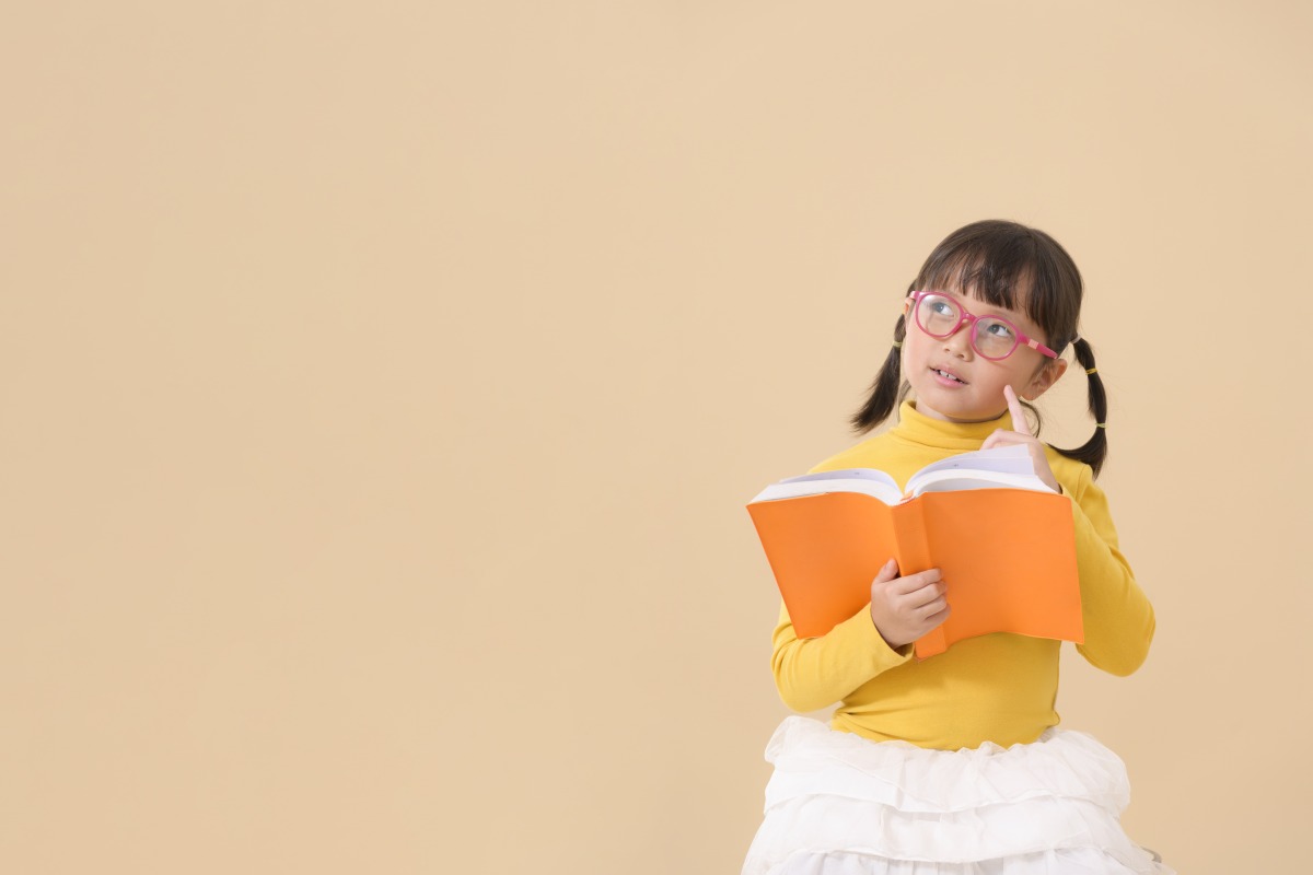 破解兒童近視迷思 國健署:戴眼鏡、成年後做雷射手術非萬靈丹 adorable cheerful asian kid little girl wearing glasses reading interesting book being thinking involved education