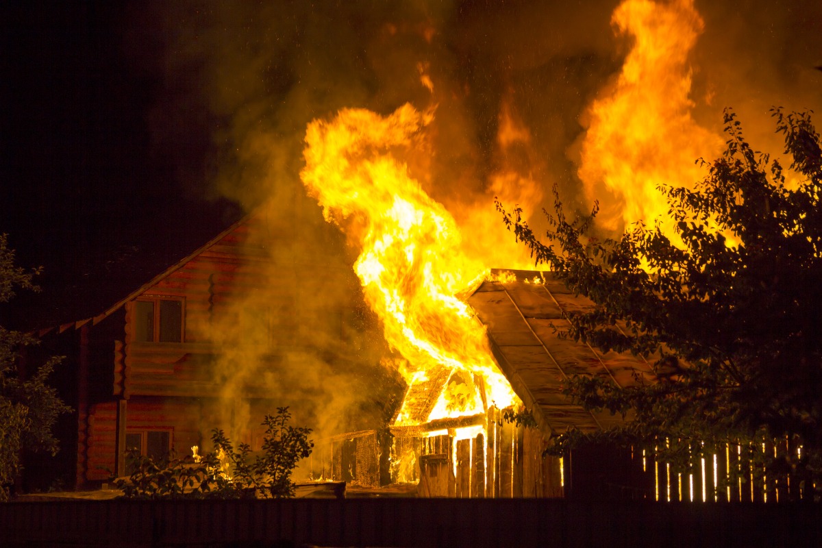 桃園男害前女友欠200萬債務 還拿私密片威脅、揚言縱火 burning wooden house night bright orange flames dense smoke from tiled roof dark sky trees silhouettes residential neighbor cottage background disaster danger concept