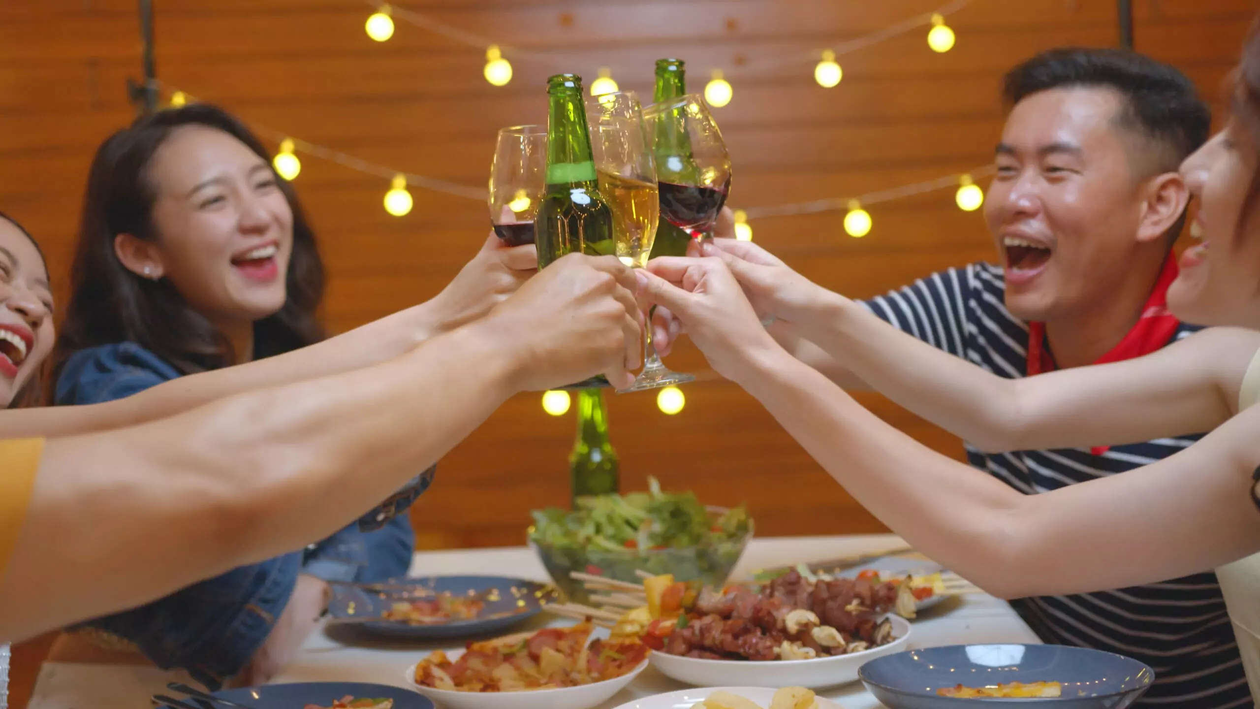 group asian people party drinking alcohol cheers beer bottle eating food sitting table scaled