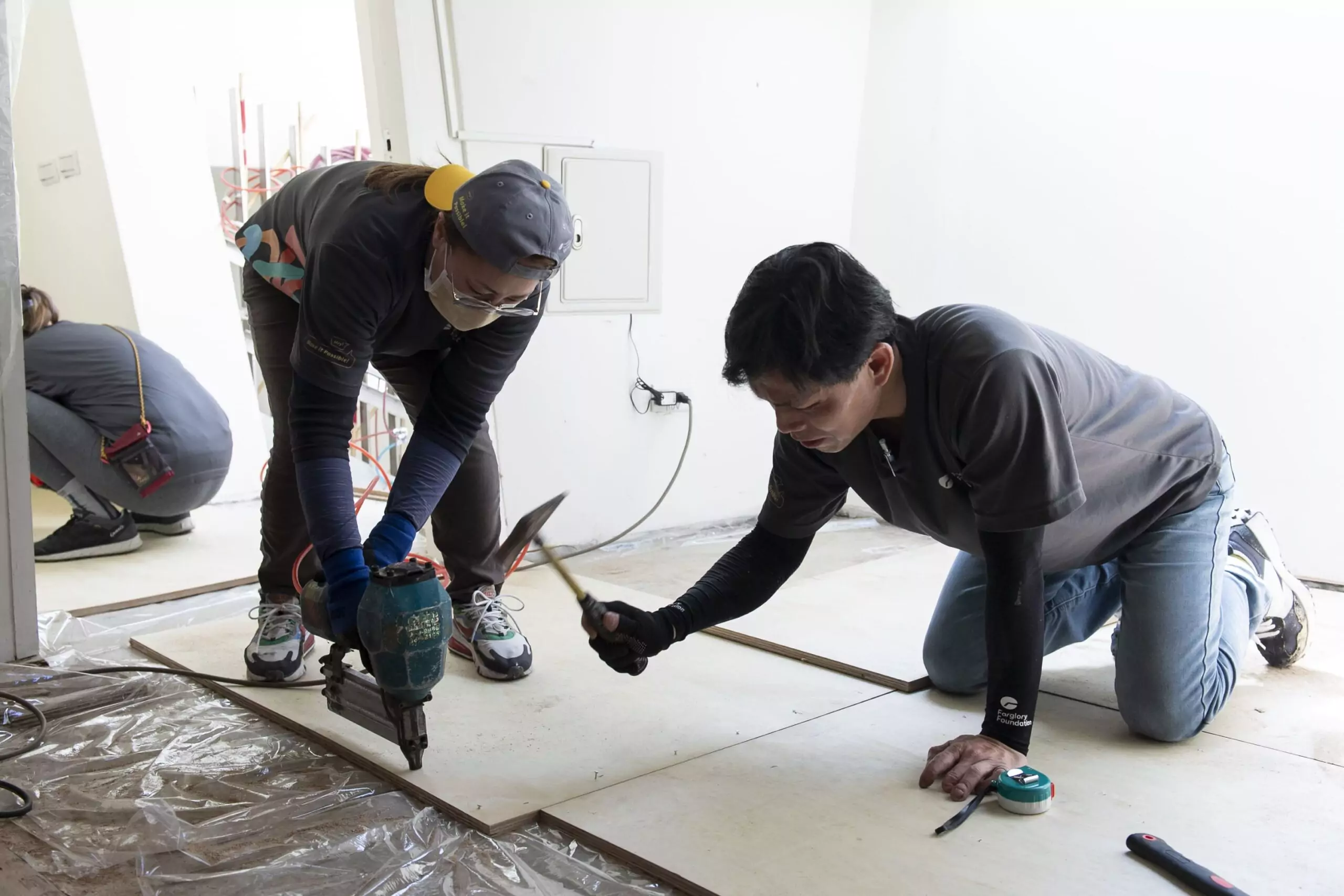 志工們在地面鋪上防潮布後，再固定夾板，以便後續工項施作 scaled